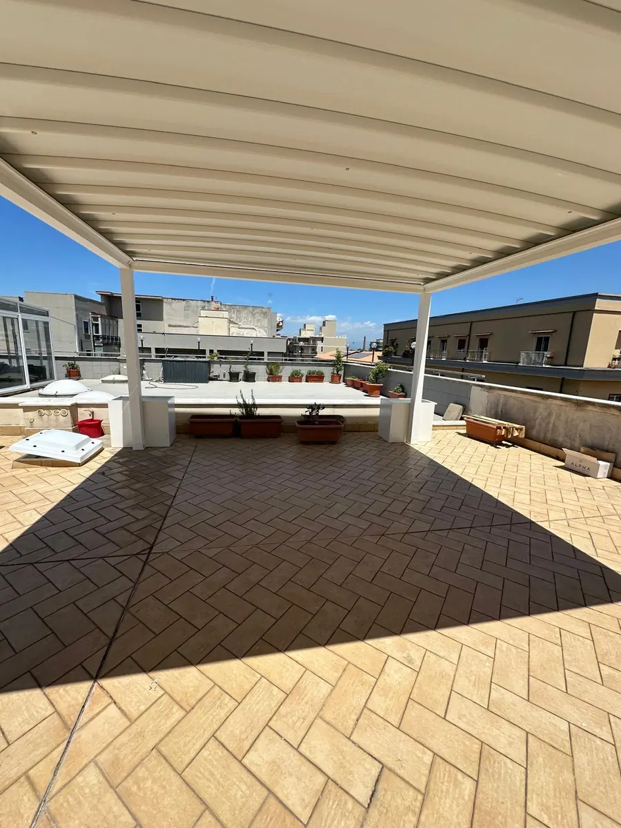 Vista interna della pergotenda chiara con telo disteso sopra il terrazzo.