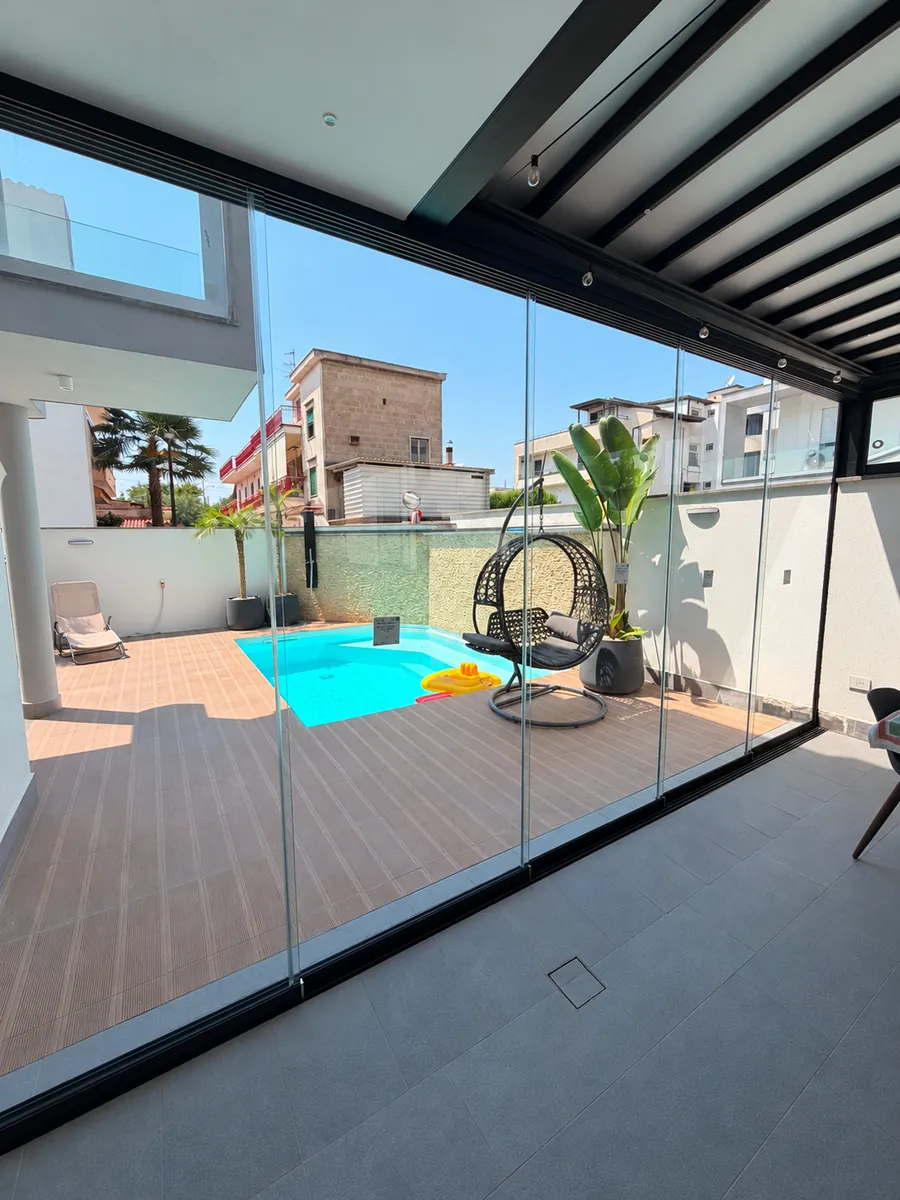 Vetrate panoramiche con profili scuri affacciate sulla piscina e sulla poltrona sospesa.