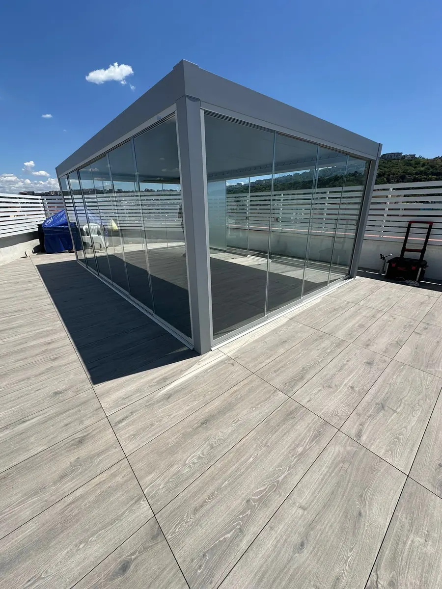 Vista esterna di una pergola chiara con chiusure panoramiche in vetro.